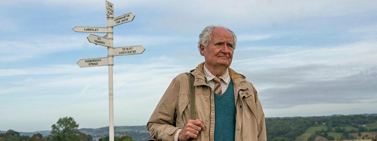 Jim Broadbent as Harold Fry stands next to a signpost in The Unlikely Pilgrimage of Harold Fry