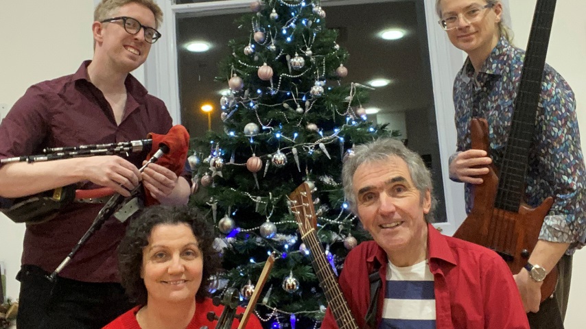Jez Lowe and his band stand around a Christmas tree in the promotional image for Jez Lowe's Get Yer Skates On.
