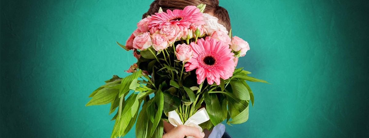 A man holds a bouquet of flowers in front of his face in a promotional image for The Importance of Being Earnest 