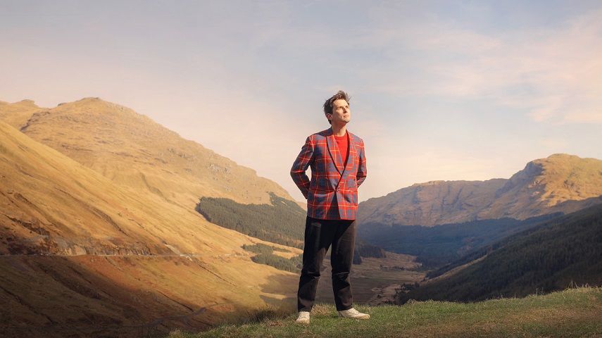 Kieran Hodgson stands with a mountain view in the background in an image for his show Big In Scotland.