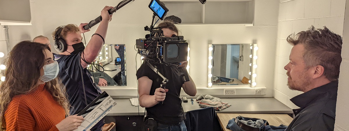 An interviewer, cameraperson and person holding a microphone boom interview someone.