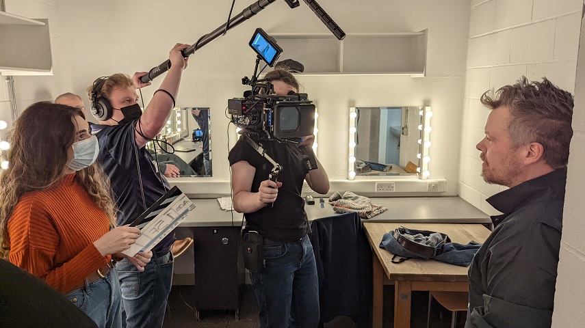 An interviewer, cameraperson and person holding a microphone boom interview someone.