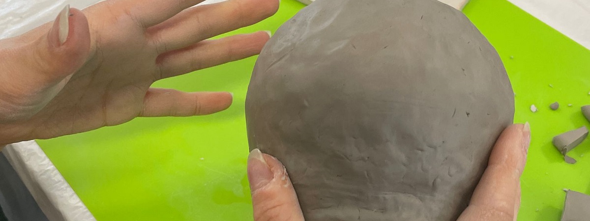 A person moulds clay into the shape of a mug.