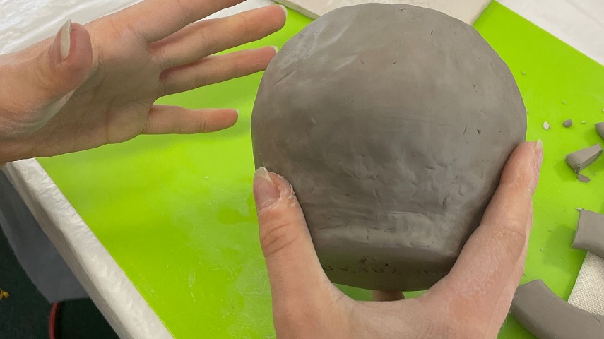 A person moulds clay into the shape of a mug.