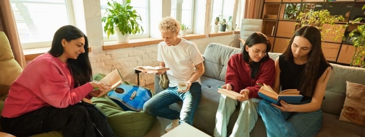 A group of people are shown with some chatting and others reading a book.