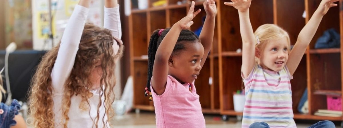 Three children have their arms in the air as they take part in a class.
